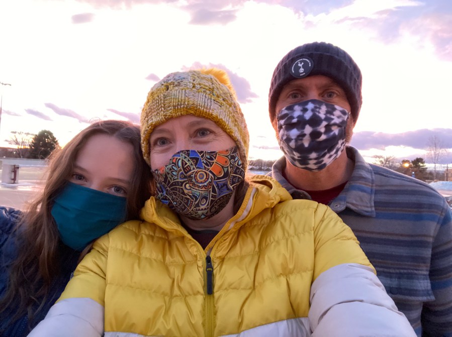 A family with masks on and a sunset behind them.