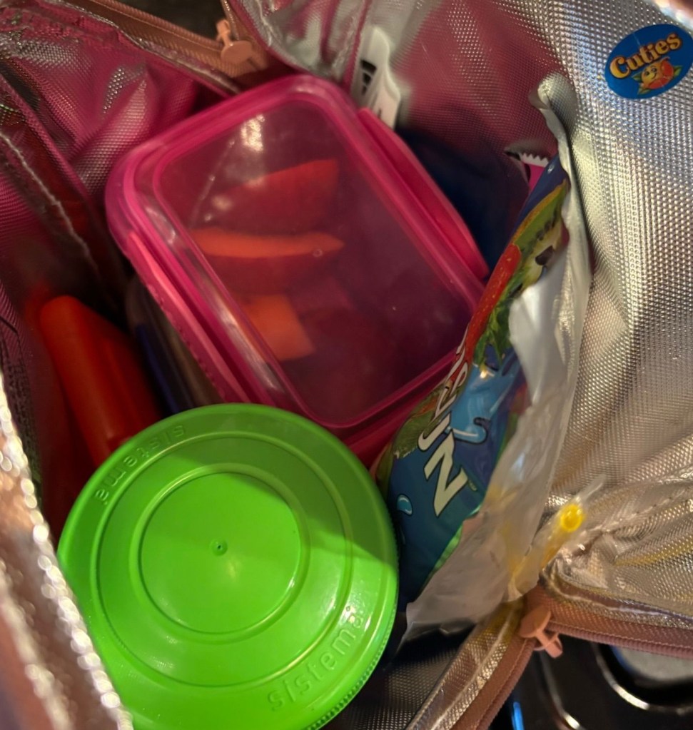 A pink soft-sided lunchbox, opened to show a Capri Sun, a green lidded container, and a pink container.